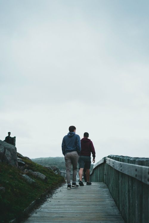 Free Two men walking down a wooden boardwalk on a cloudy day, capturing a serene outdoor moment. Stock Photo