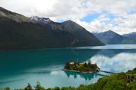 在晴朗的夏日天空下，山间宁静的湖泊倒映着云彩和绿叶