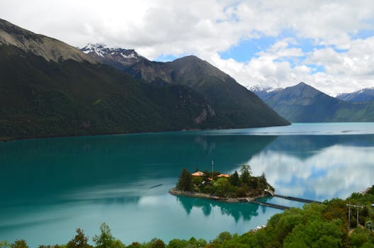 在晴朗的夏日天空下，山间宁静的湖泊倒映着云彩和绿叶