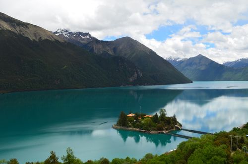 Free A tranquil lake in the mountains reflecting clouds and greenery under a clear summer sky. Stock Photo