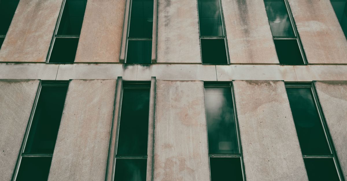 A modern concrete building facade with repetitive windows creating a minimalistic architectural pattern.