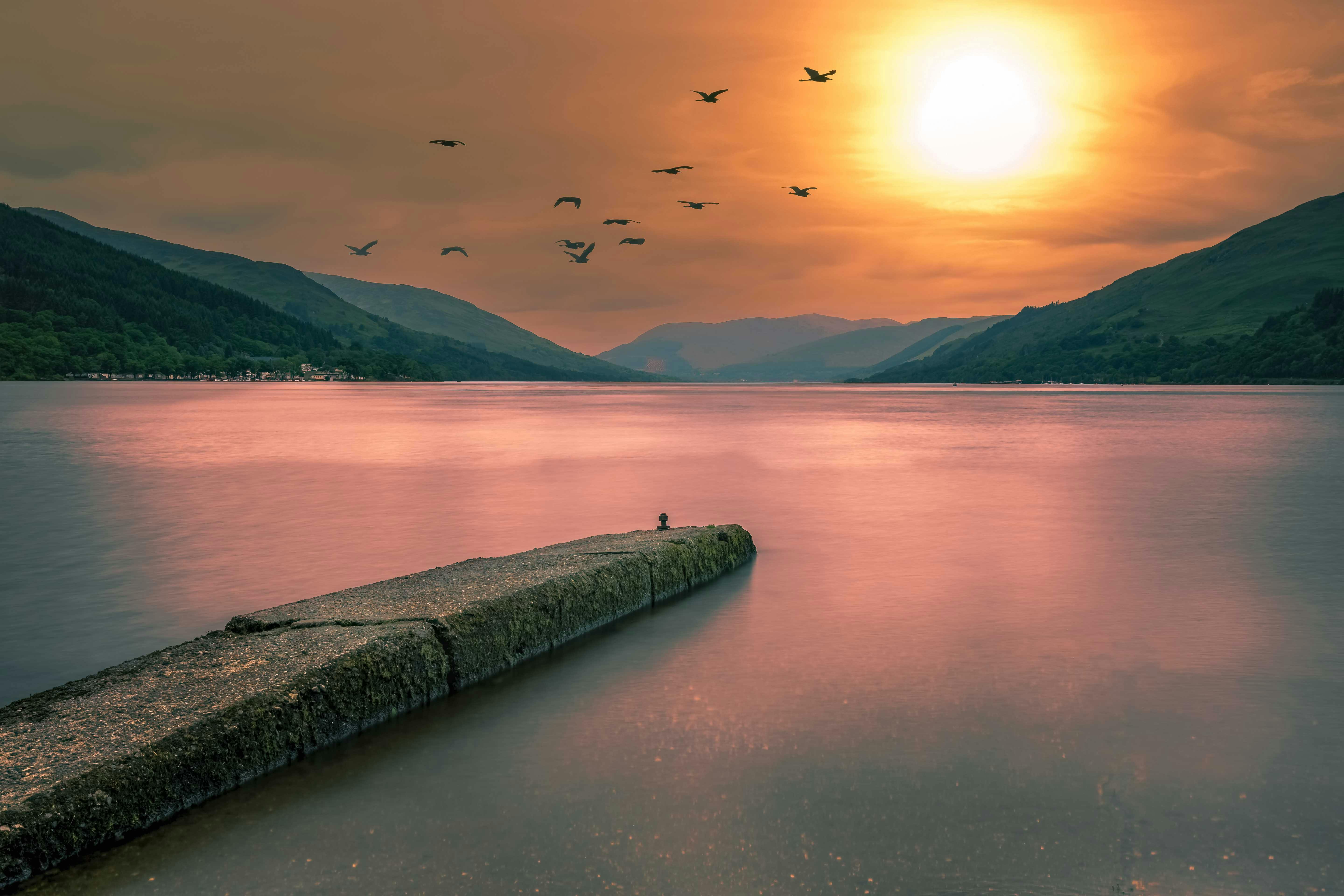 A tranquil sunset over a loch in Glencoe, Scotland with birds in the sky.