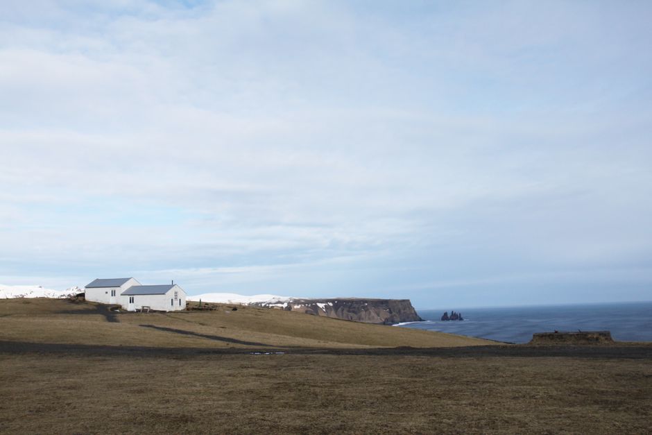 A serene coastal scene with a white house on Iceland's cliffs overlooking the ocean.