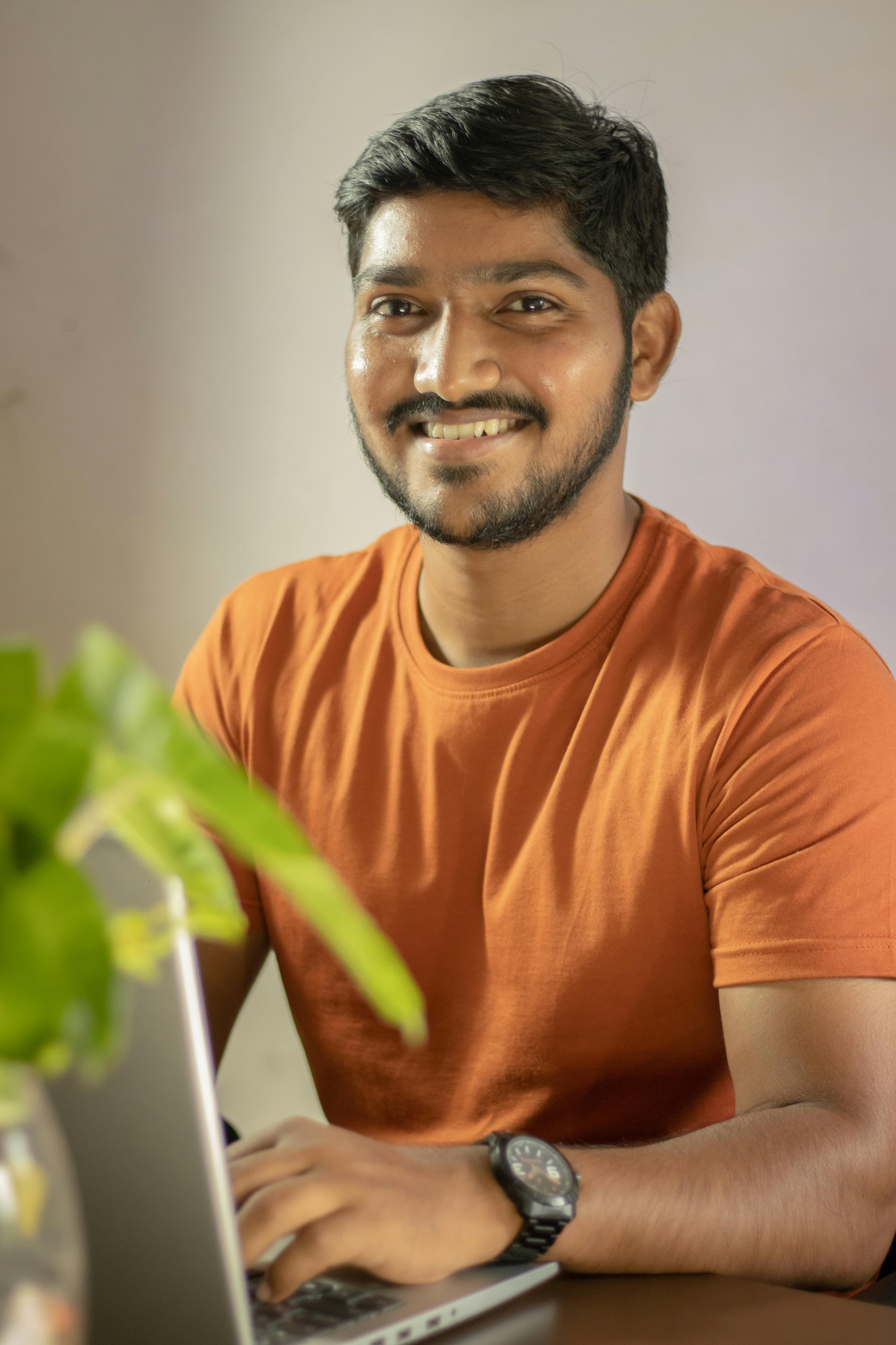 Man in an orange shirt enjoying remote work from home setup with a laptop.