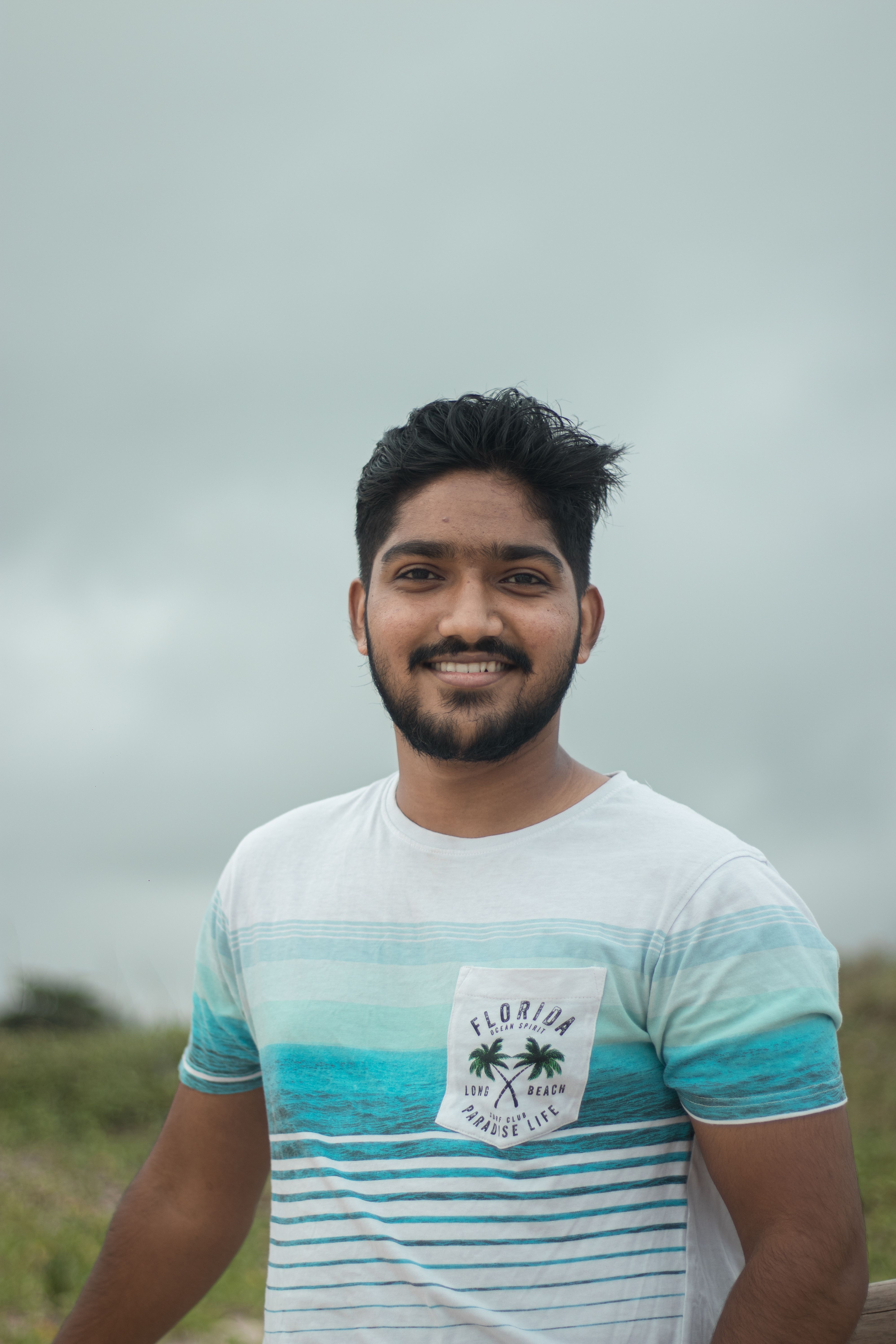 Portrait of a happy man in casual wear smiling outdoors against a cloudy sky.