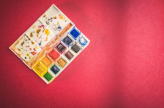A top view of a vibrant watercolor paint set on a textured red background, perfect for creativity.