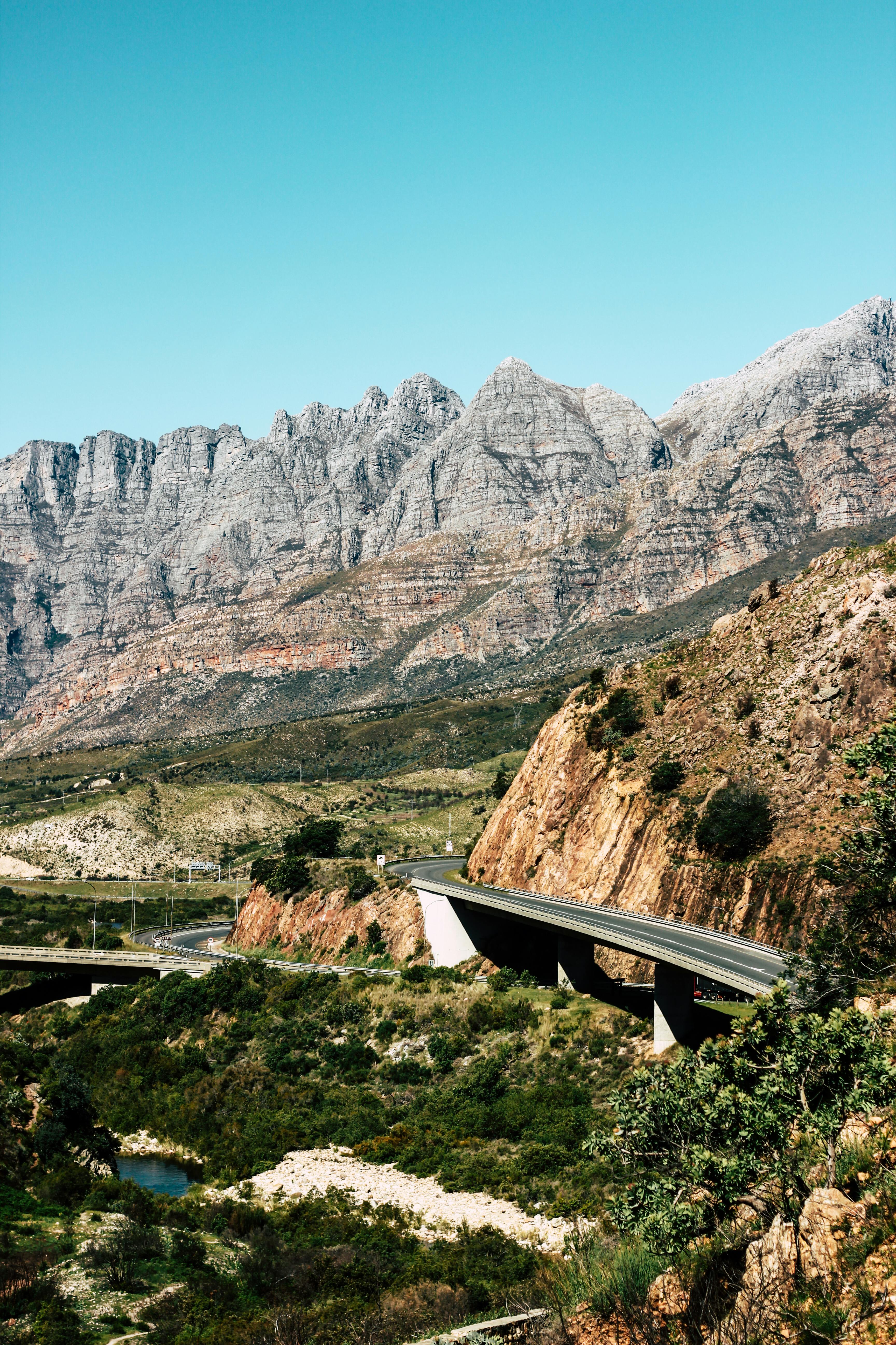 在晴朗的蓝天下，公路桥穿越崎岖山脉的景色十分迷人