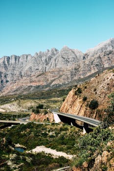 在晴朗的蓝天下，公路桥穿越崎岖山脉的景色十分迷人
