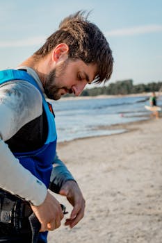 A man in a wetsuit prepares for water activities on a sunny beach.