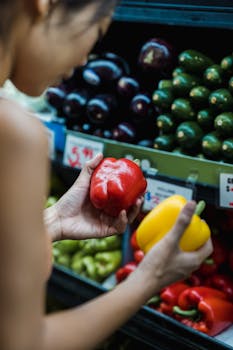 A woman chooses between red and yellow bell peppers at a supermarket shelf.