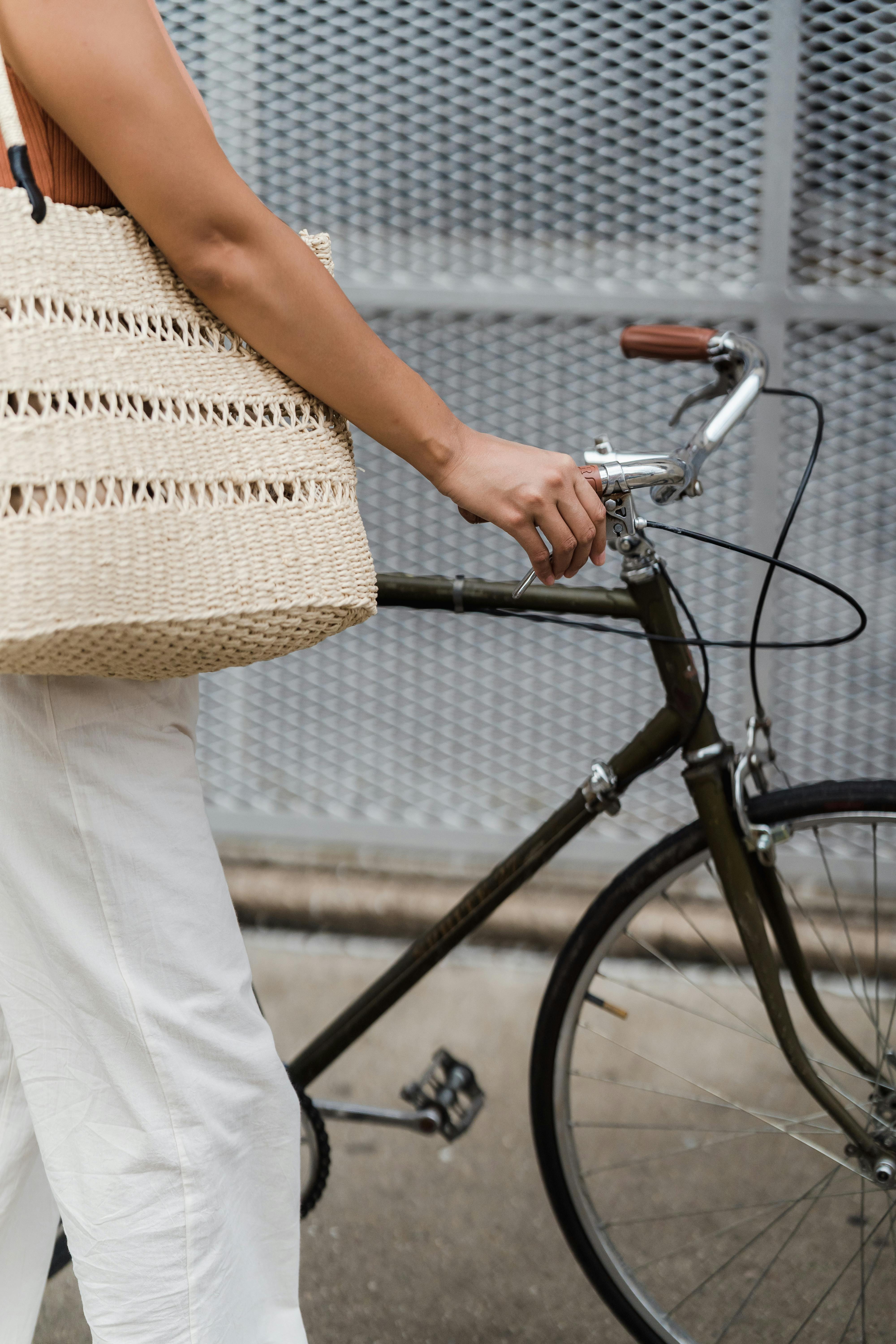 Close-up of a woman holding a bicycle handle while carrying a stylish wicker bag outdoors.