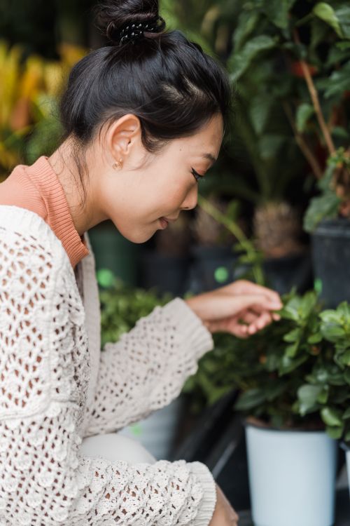 Free Side profile of a woman in a white cardigan interacting with potted plants. Stock Photo