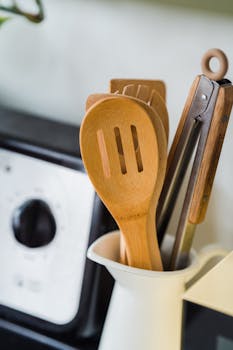 Close-up of wooden and metal kitchen utensils in a white container on a kitchen countertop.