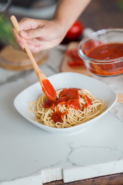 A Person Putting Tomato Sauce in a Pasta