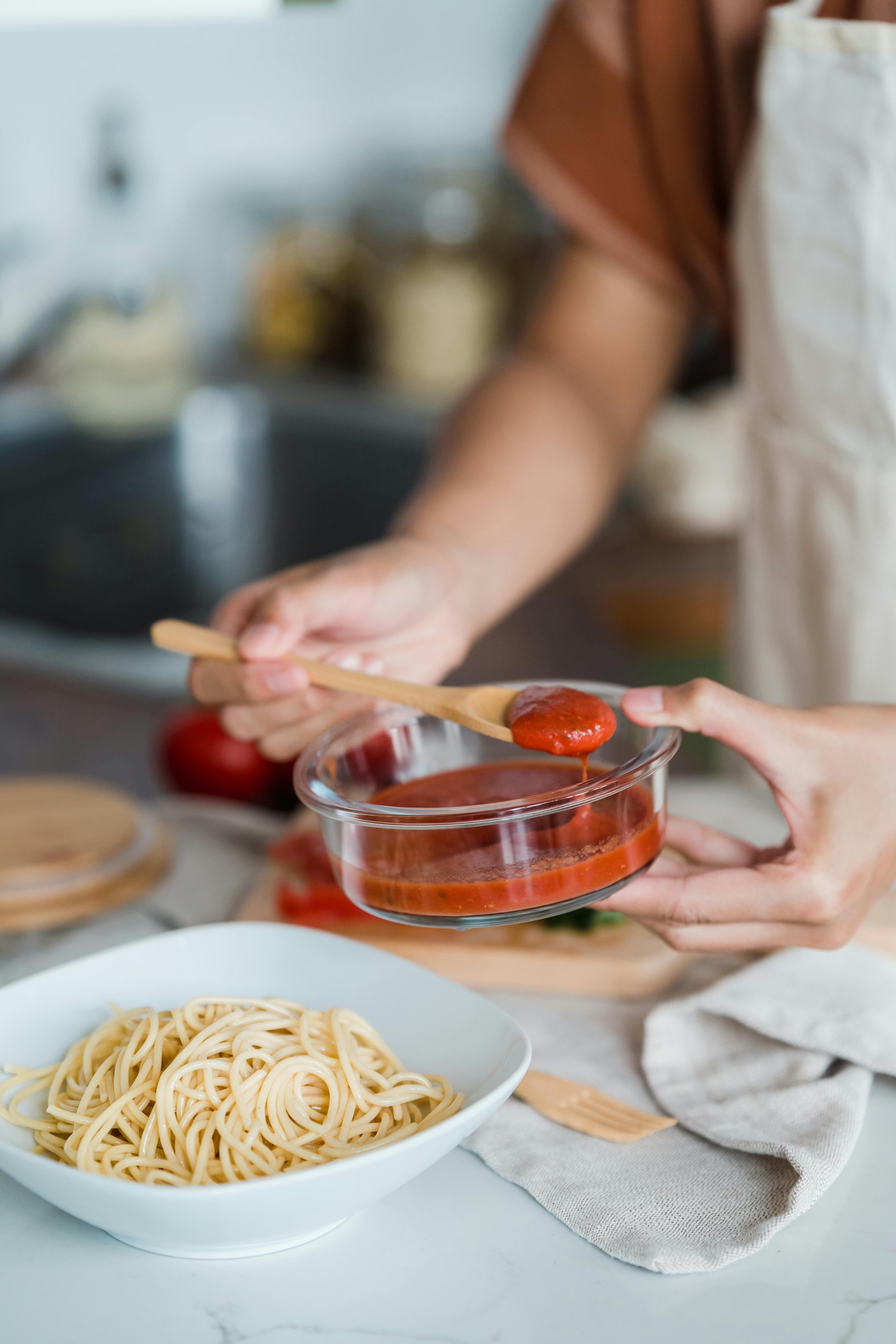Free A Person Putting Tomato Sauce in a Pasta Stock Photo
