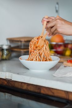 A delicious bowl of spaghetti being prepared on a kitchen counter, showcasing a fresh meal.