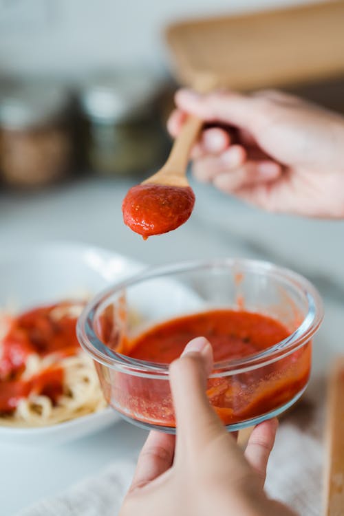Close-Up Photo of a Person Holding a Food Container and Wooden Sauce with Tomato Sauce