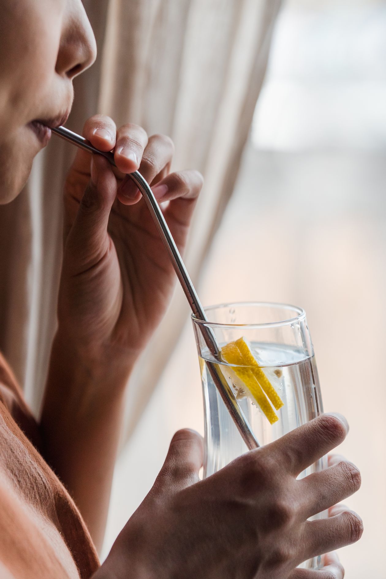 Person sipping lemon water through a metal straw to stay hydrated throughout the day