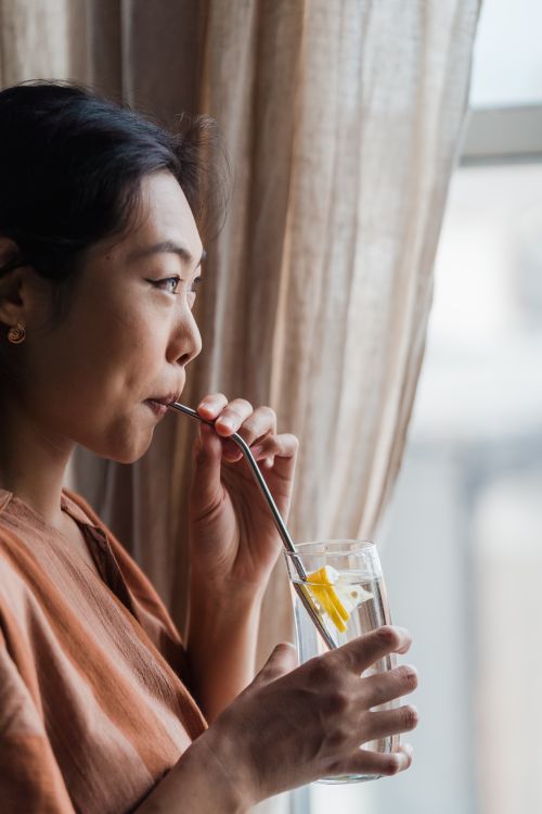 Free Asian woman sipping lemon water through a metal straw indoors, embracing a healthy lifestyle. Stock Photo