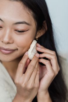 Close-up of an Asian woman smiling while applying facial care product.