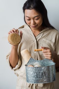 A woman holding a dry brush and clean toiletries in a textured metal bucket labeled 'CLEAN'.