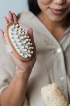 A woman holding a wooden massage brush emphasizing personal hygiene and skincare.