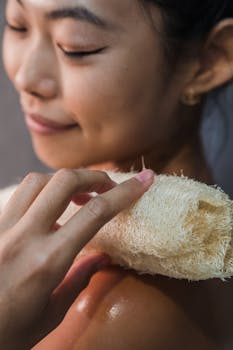 Close-up of a woman gently scrubbing her shoulder with a loofah for skincare.