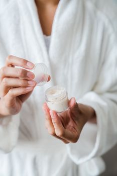 Close-up of hands holding a jar of moisturizer, highlighting skincare routine.