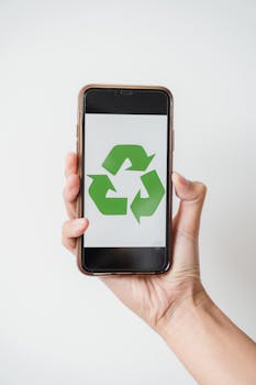 Close-up of hand holding smartphone displaying green recycling symbol on screen.