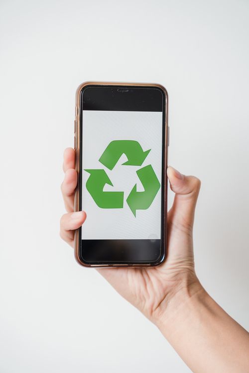 Free Close-up of hand holding smartphone displaying green recycling symbol on screen. Stock Photo