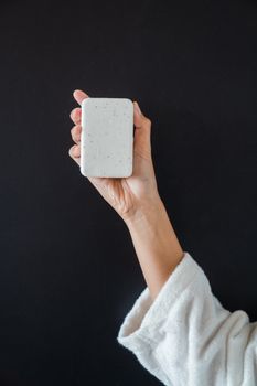 Close-up of a hand in a robe holding a bar of white soap against a black background, symbolizing cleanliness.