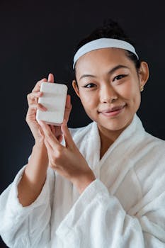 Smiling woman in bathrobe holding bar soap, promoting personal hygiene.