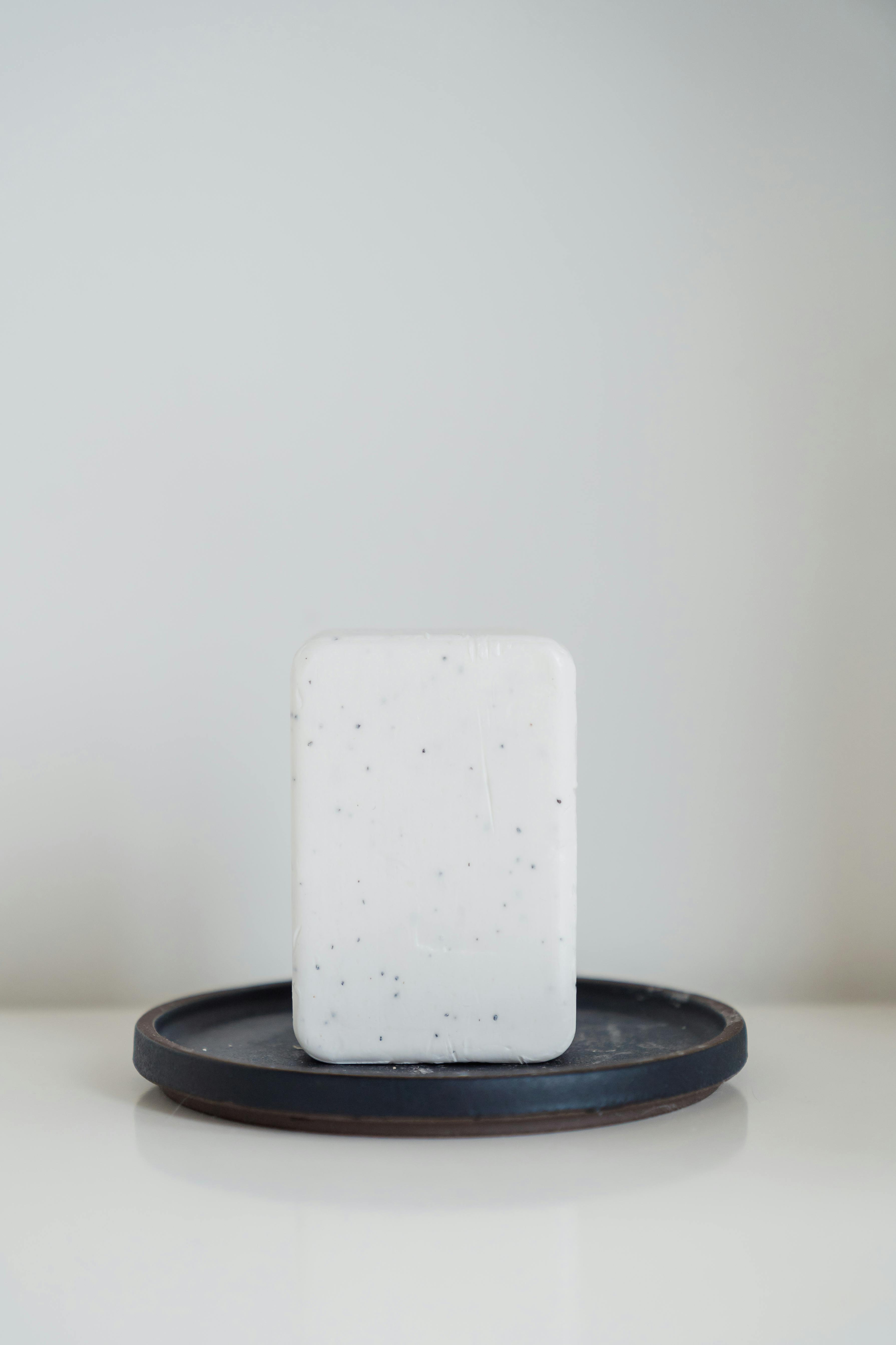 Simple and clean bar soap placed on a dark round tray against a white background.