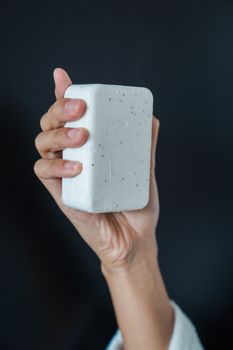 Detailed close-up of a woman's hand holding a white bar of soap against a dark background.