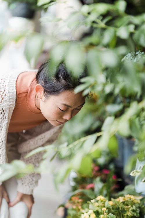 Free A woman in a white cardigan curiously looking at flowers in a lush garden. Stock Photo
