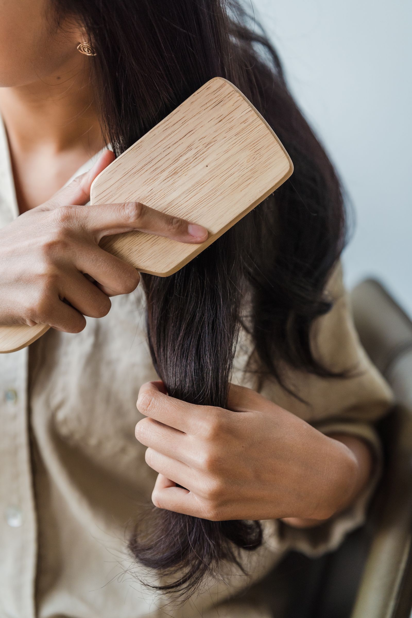 Close-up of a woman gently brushing long dark hair, illustrating natural hair regrowth care