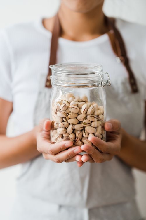 Free A close-up view of hands holding a jar filled with shelled pistachios, showcasing healthy eating. Stock Photo
