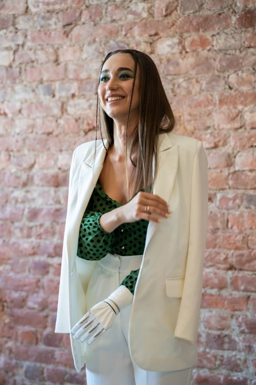 Free Confident woman with prosthetic arm in a white suit smiles against a brick wall. Stock Photo