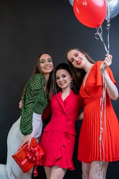 Three women in stylish dresses celebrating with balloons, exuding joy and elegance.