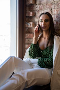 Elegant woman with a prosthetic hand talking on the phone by the window.