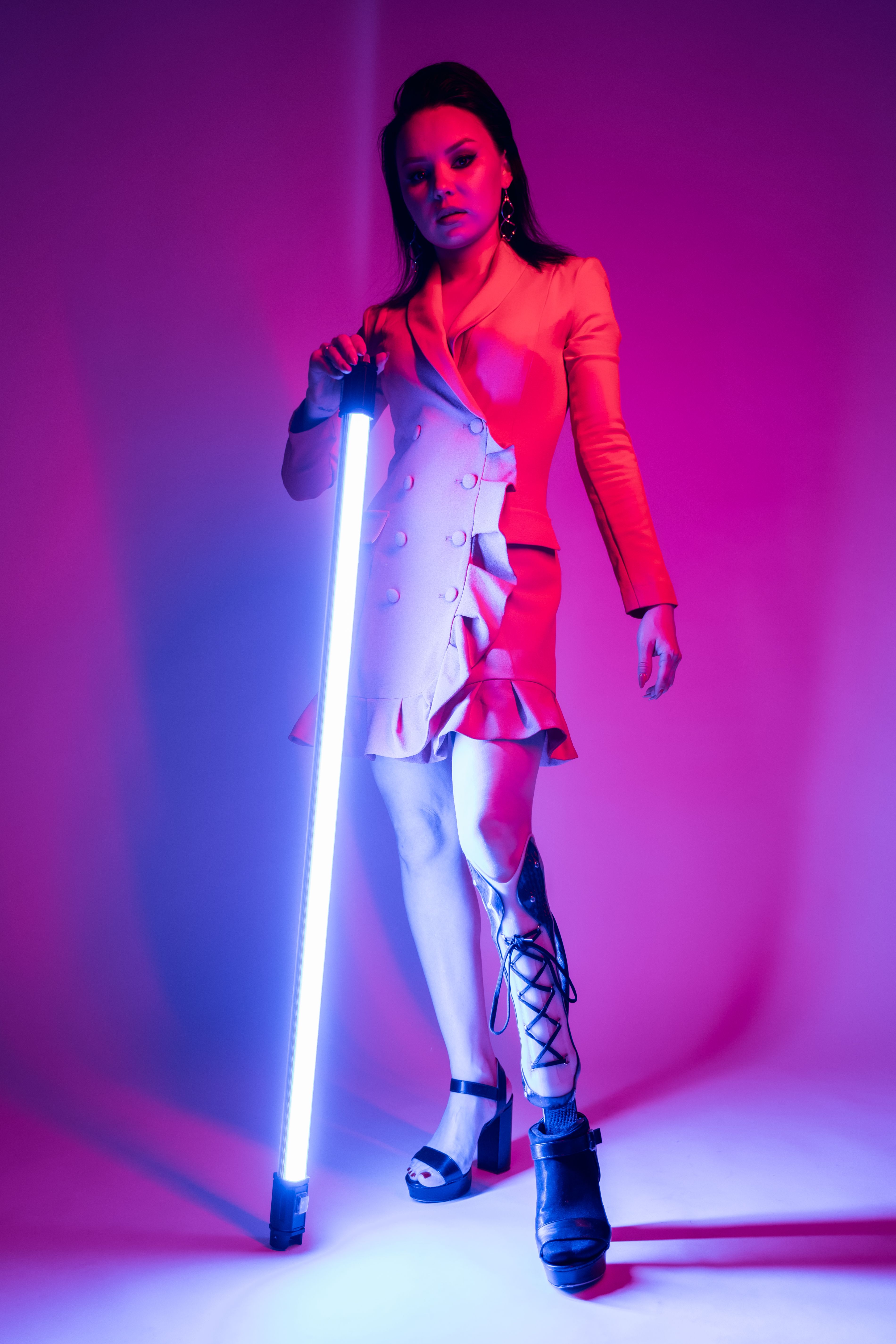 Fashionable woman with a prosthetic leg stands confidently under vibrant neon lighting.