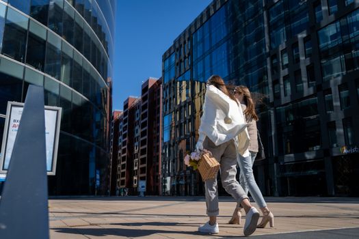 Woman in White Long Sleeve Shirt and White Pants Holding Brown Leather Bag Walking on Sidewalk