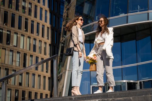 Free Two stylish women with a basket of flowers enjoying a sunny urban day, showcasing modern fashion. Stock Photo