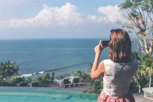 Woman Wearing White and Red Sleeveless Dress Taking Photo of Beach