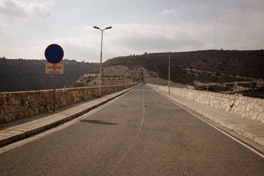 A wide, empty mountain road with 'No Parking' signs under a cloudy sky in Cyprus.