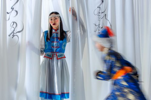 Free Two individuals in Mongolian clothing captured amidst flowing curtains, blending tradition with dynamic motion. Stock Photo