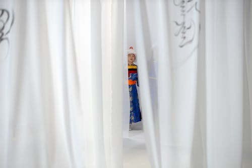 Man in a Traditional Dress Peaking Through Curtains