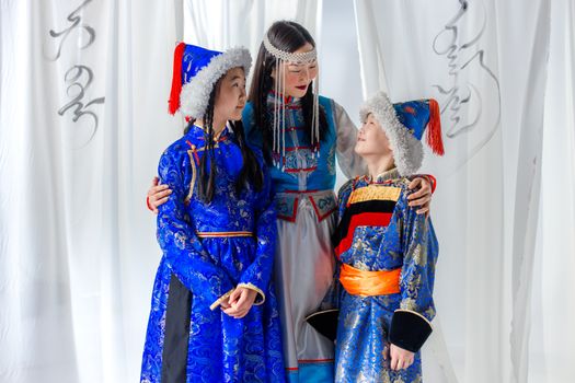Three smiling family members wearing traditional Mongolian clothing indoors.