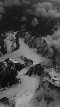 A striking black and white aerial view of snow-covered peaks and glaciers above the clouds.