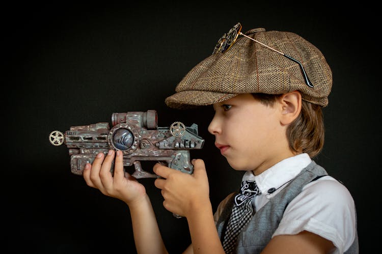 A Kid Wearing Ivy Cap Holding An Rusty Toy Gun